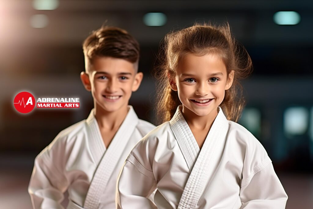 Two young children, a boy and a girl, dressed in white Karate uniforms with belts, smiling confidently at the camera. Their expressions reflect the joy and confidence they've gained through martial arts training, emphasizing the positive impact of Karate on children's development.